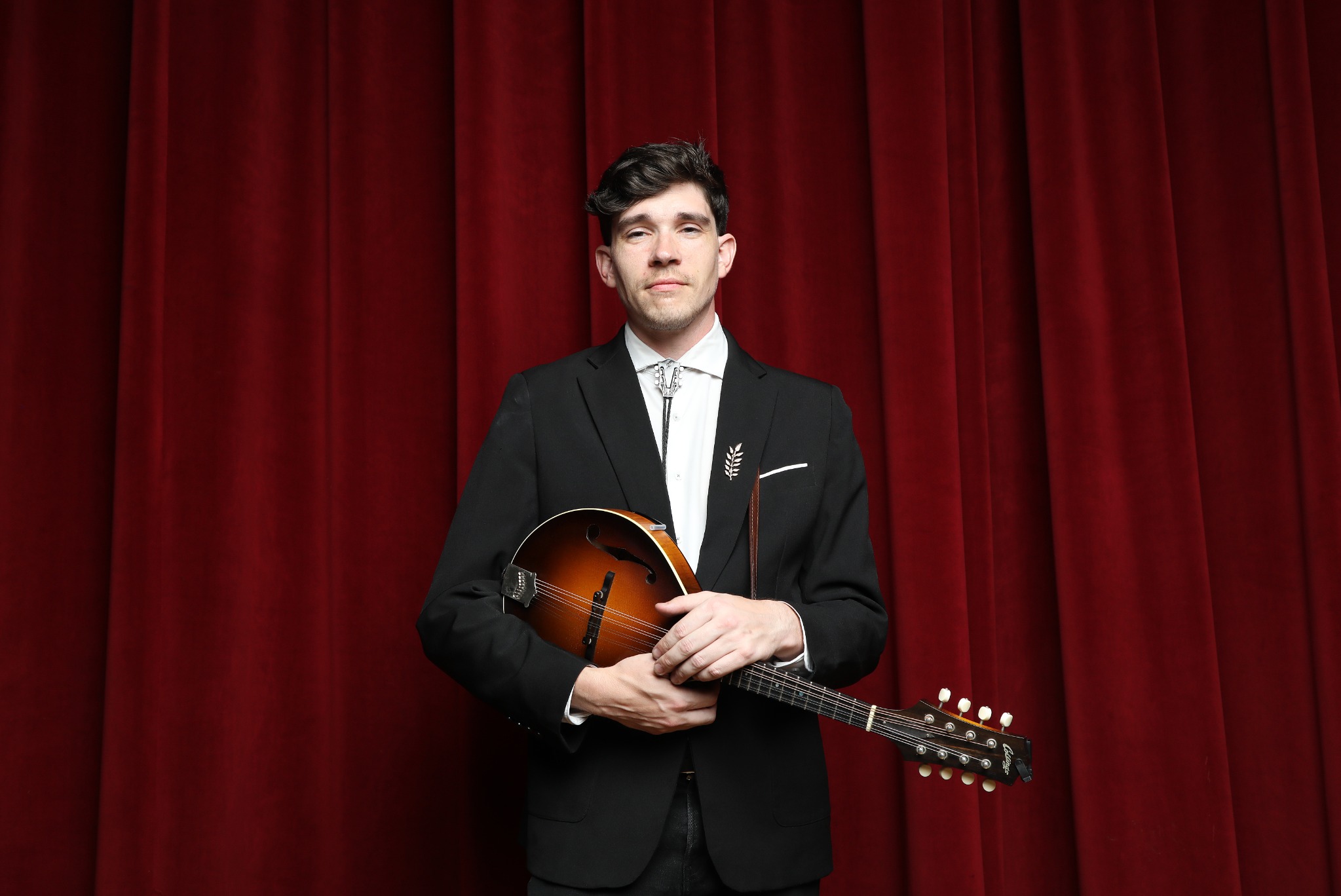 John Seltzer holding mandolin against a red curtain